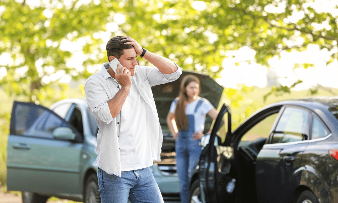 man on phone holding head next to car crash