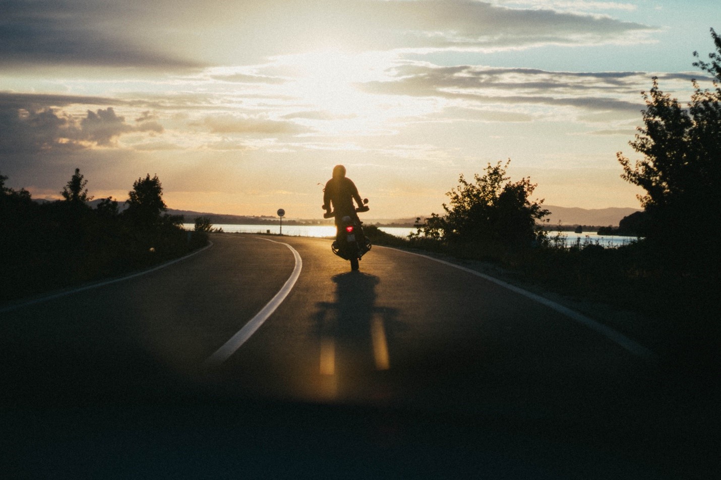 motorcyclist riding on road at sunset