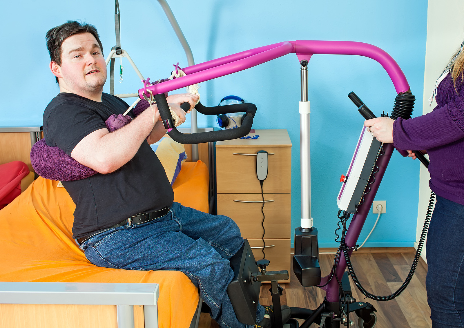 Spastic young man with infantile cerebral palsy caused by complications at birth using a patient lift to hoist himself out of a healthcare bed for transfer to a multifunctional wheelchair