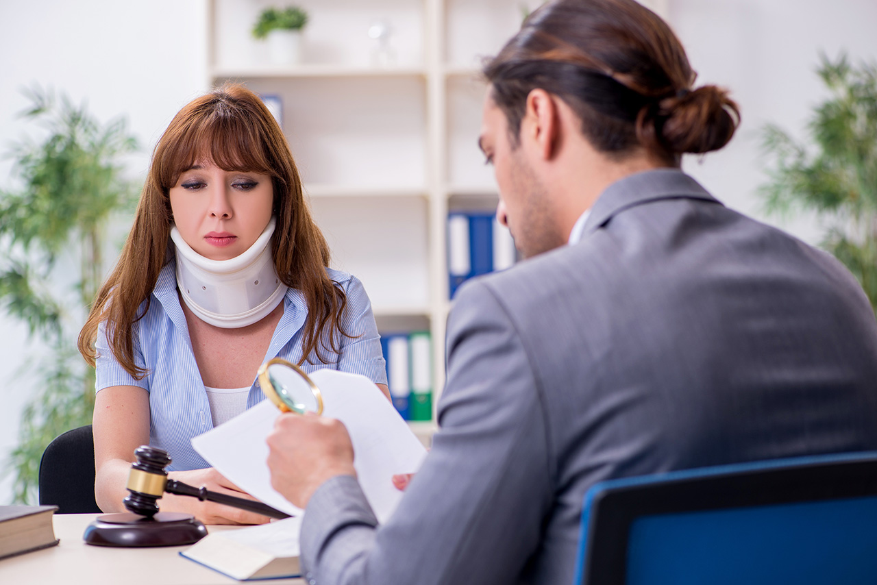 Young whiplashed injured woman and male lawyer reviewing paperwork