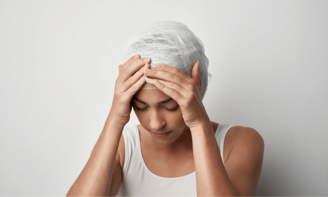 young woman head wrapped in white bandage holding head with both hands