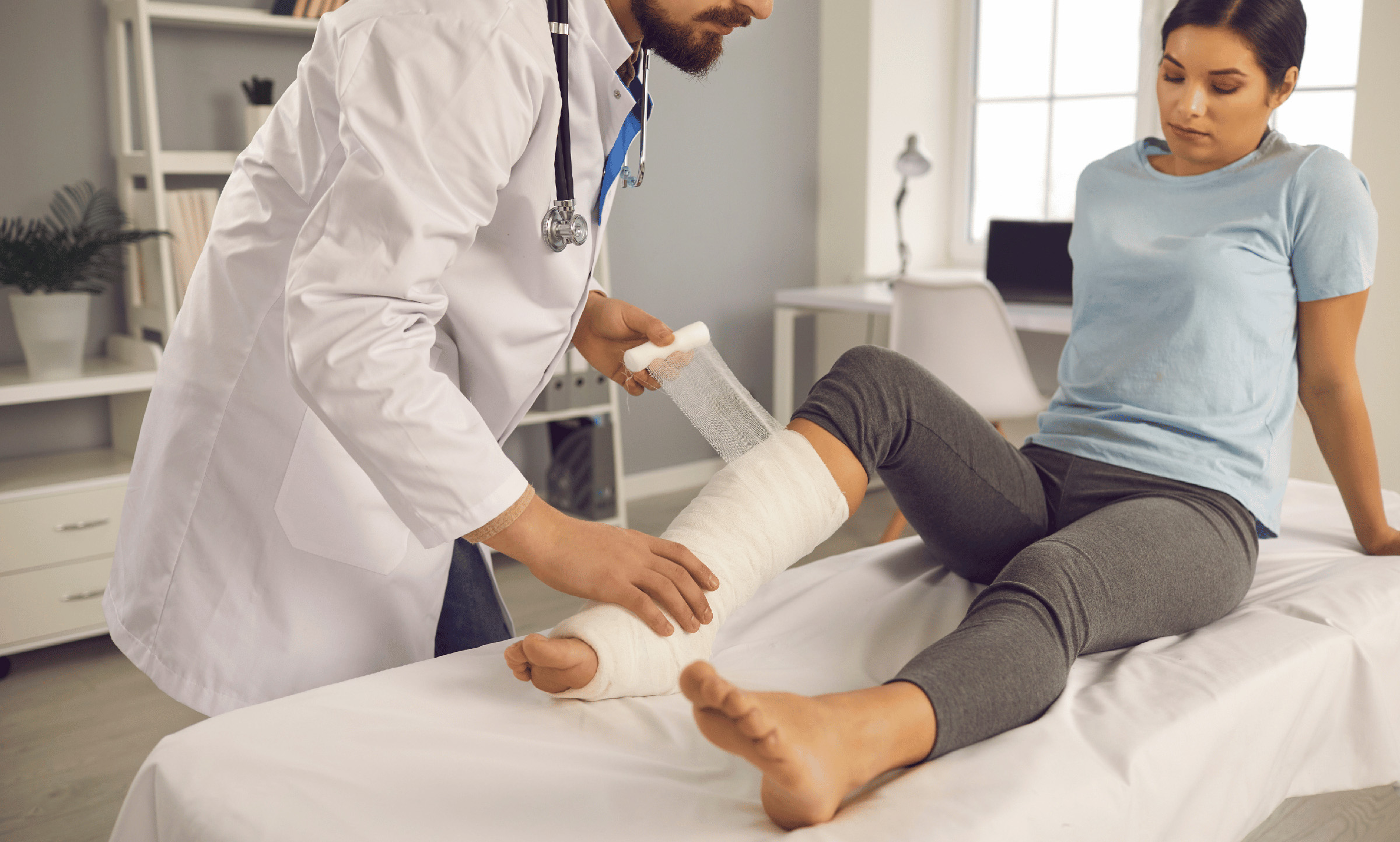 Woman in emergency room with broken leg on stretcher attended by physician.