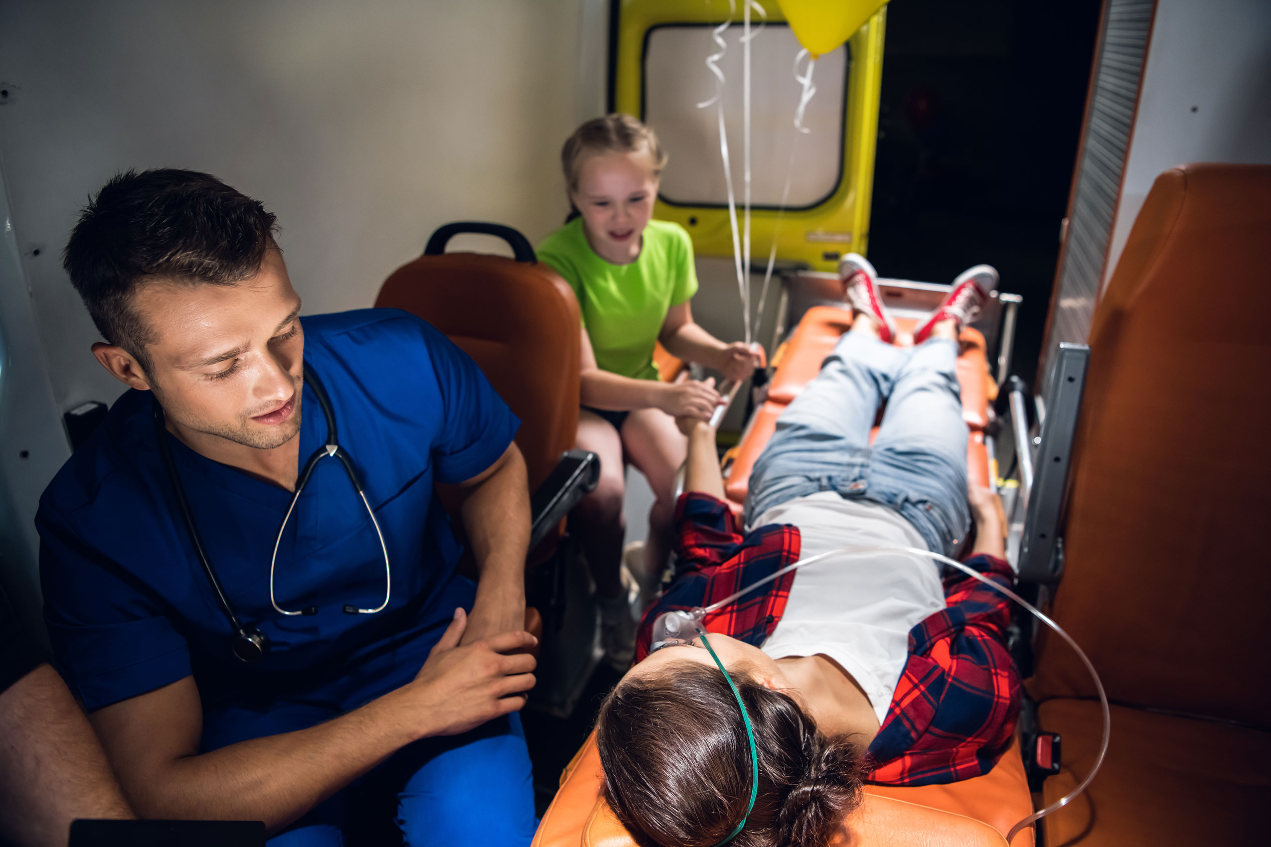 A Young Mother Got Into An Amusement Park Accident and is in the ambulance with her young daughters holding her hand.