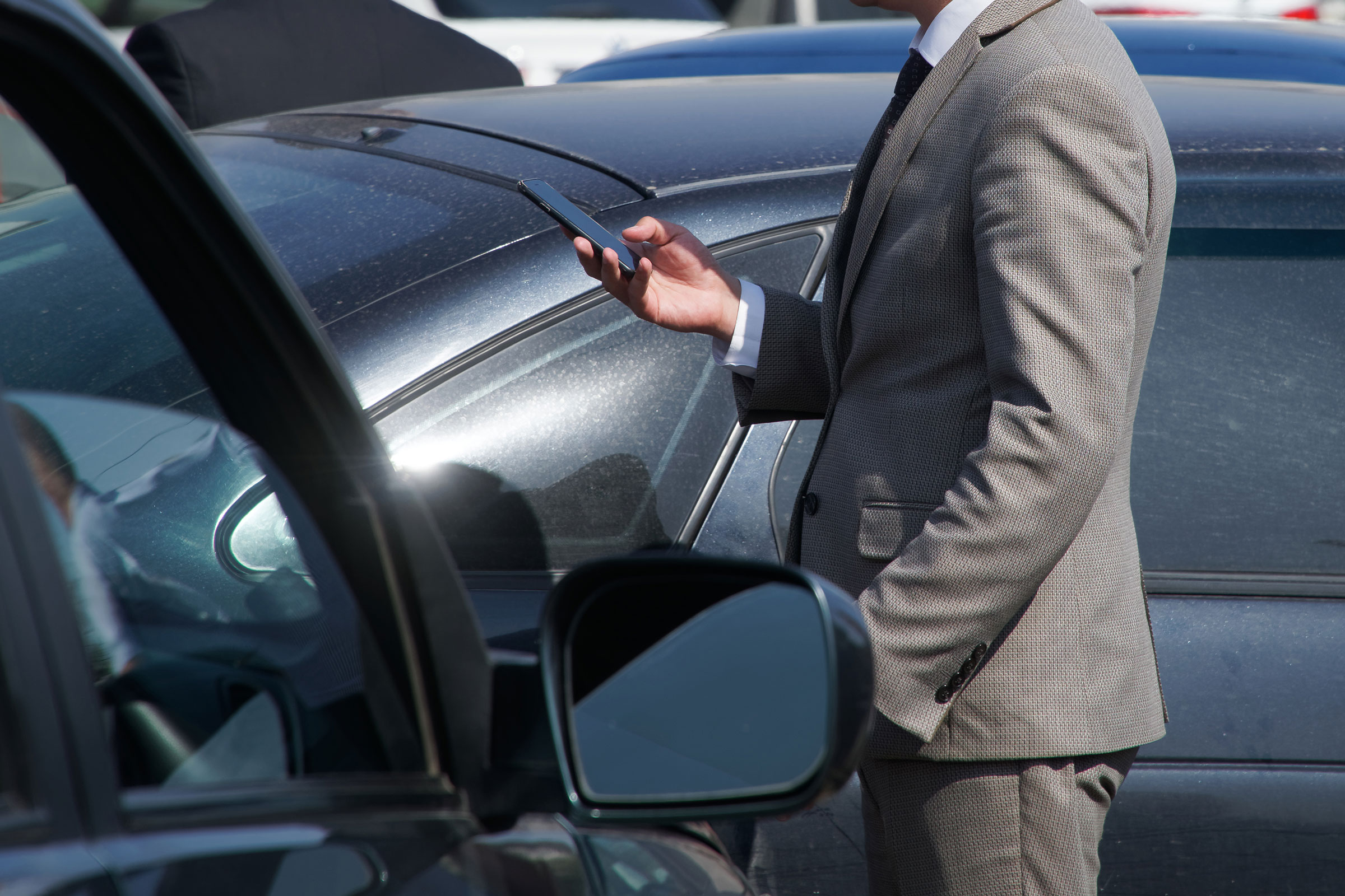 a man in a business suit at the scene of a car accident using his smart phone