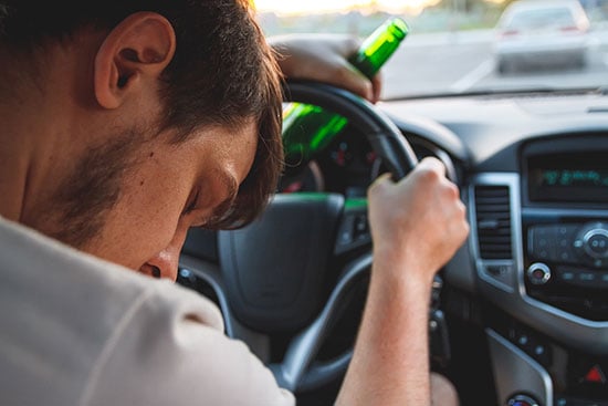 Intoxicated driver passed out at steering wheel holding a bottle of beer