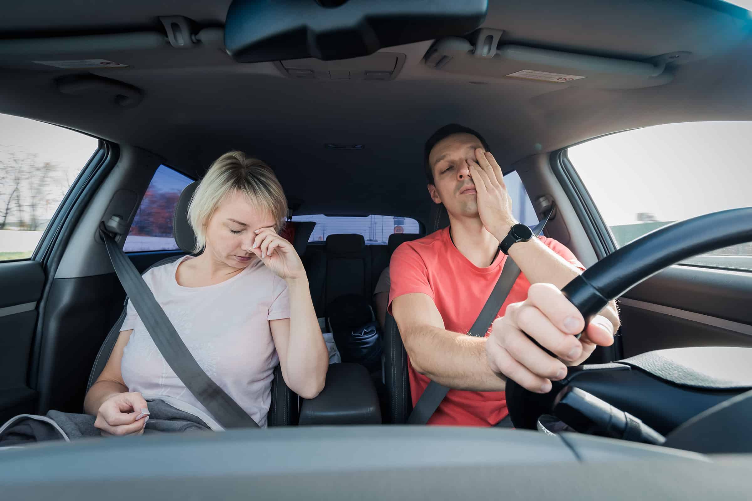 tired woman passenger and man driving falling asleep at the wheel