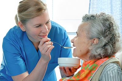 staff feeding elderly woman nursing home patient