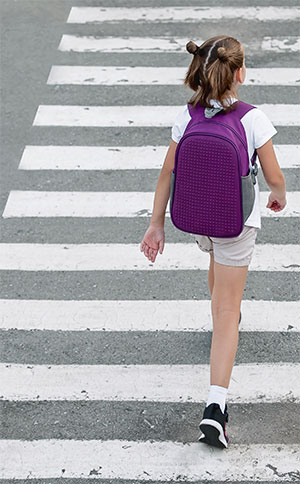 Young school girl crossing street at crosswalk on way to school