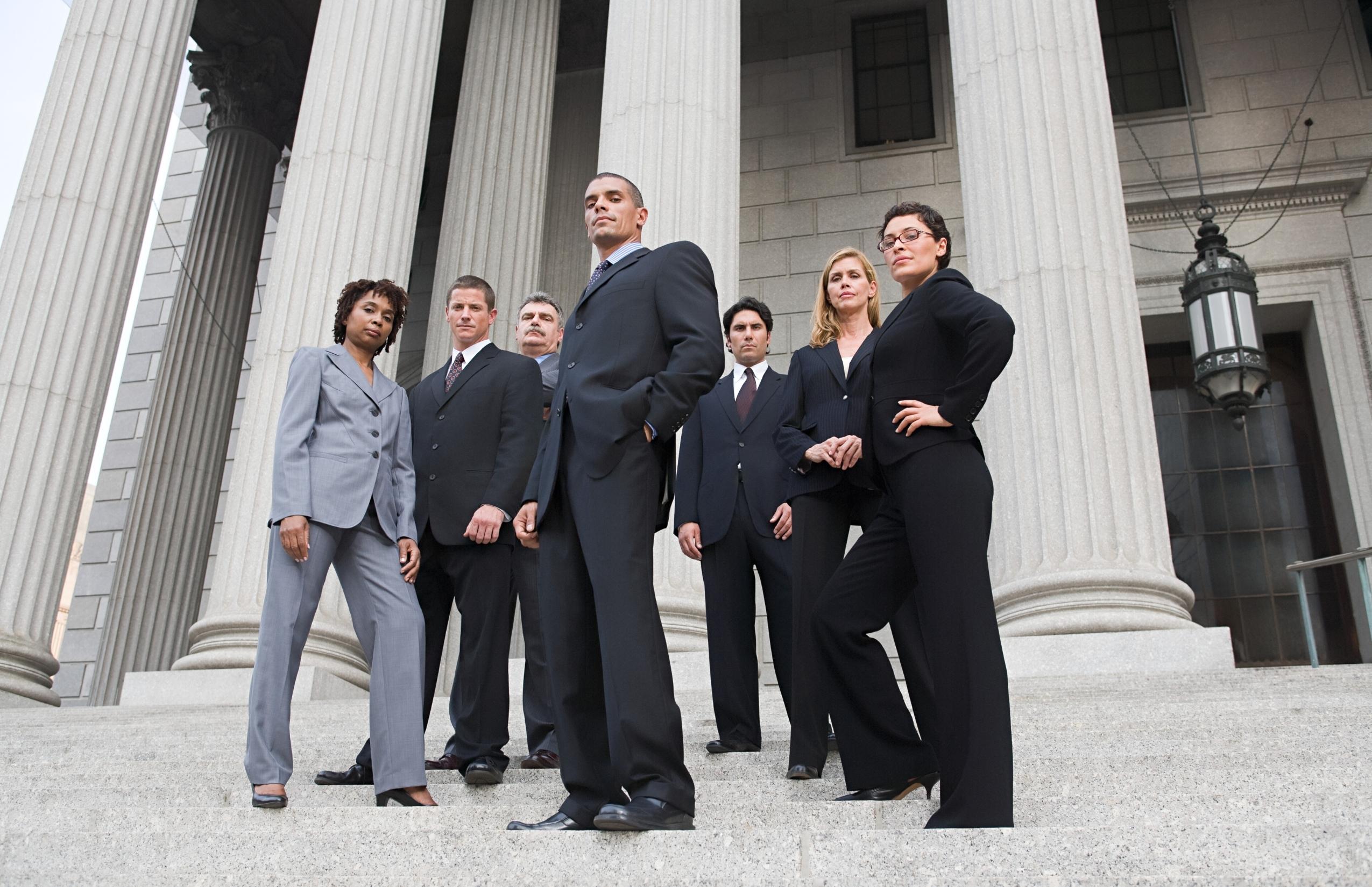 Group of lawyers standing outside on courhouse steps in front of three large cement columns