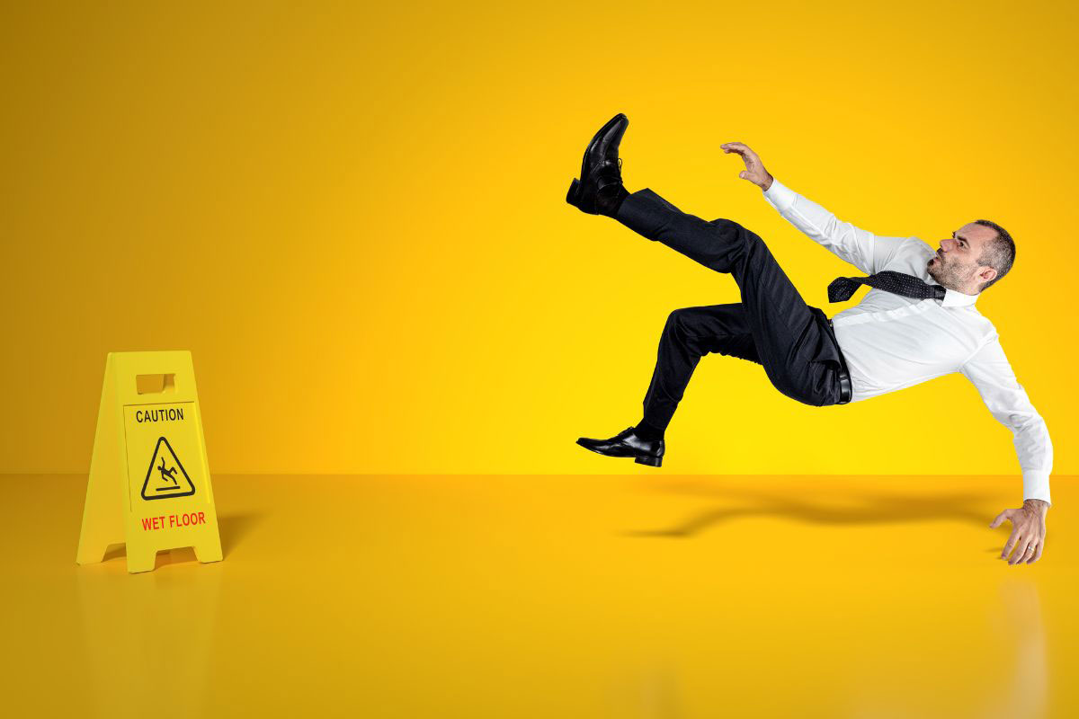 man slippiing near wet floor sign yellow background