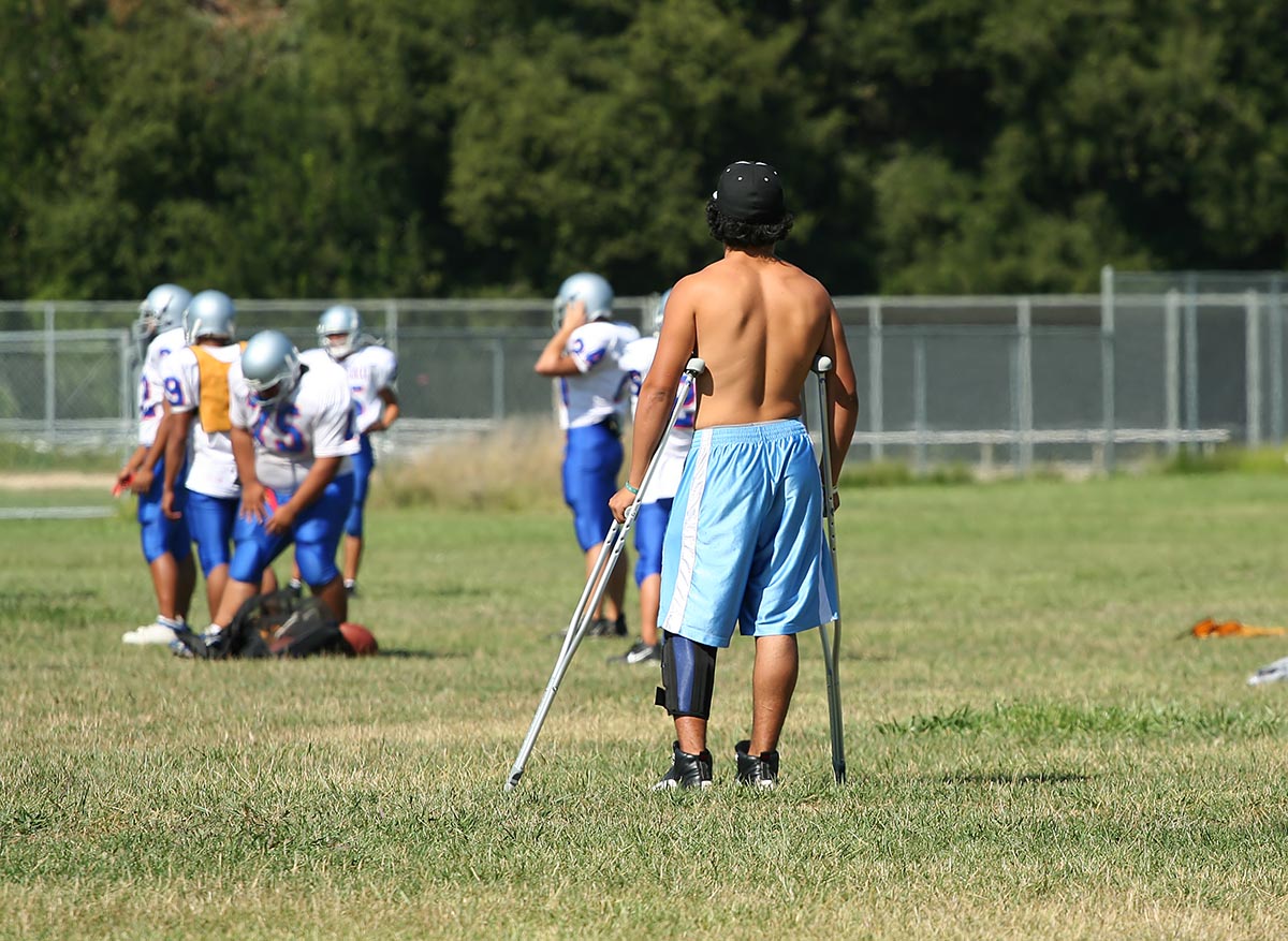 Injured teen on crutches watching team mates play football